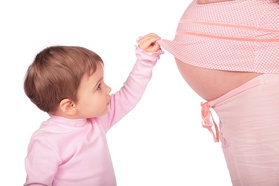 a photo of a toddler lifting a woman's shirt to reveal her pregnant belly